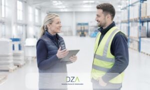 Personaldisponentin bespricht mit Zeitarbeitskraft in Warnweste den Einsatz und die arbeitsmedizinische Vorsorge im Lager